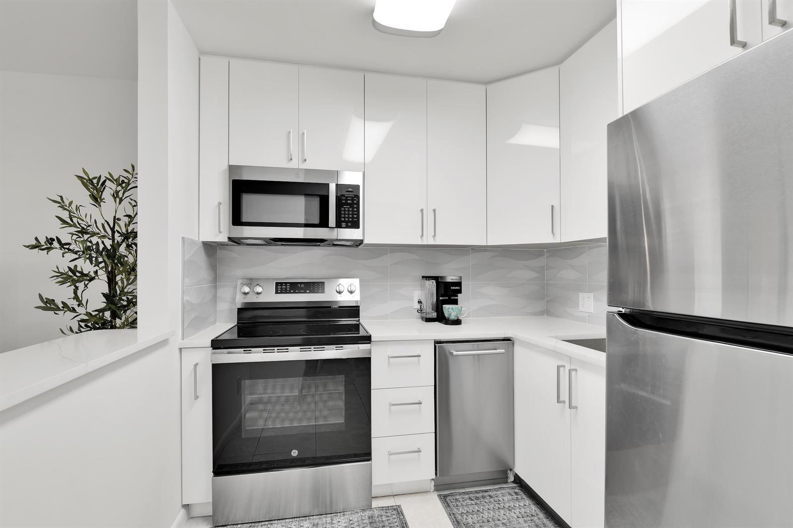 A modern kitchen features white cabinets, stainless steel appliances, and a patterned tile backsplash — 175 Fanshaw E, Boca Raton FL 33434, BOCA RATON, FL