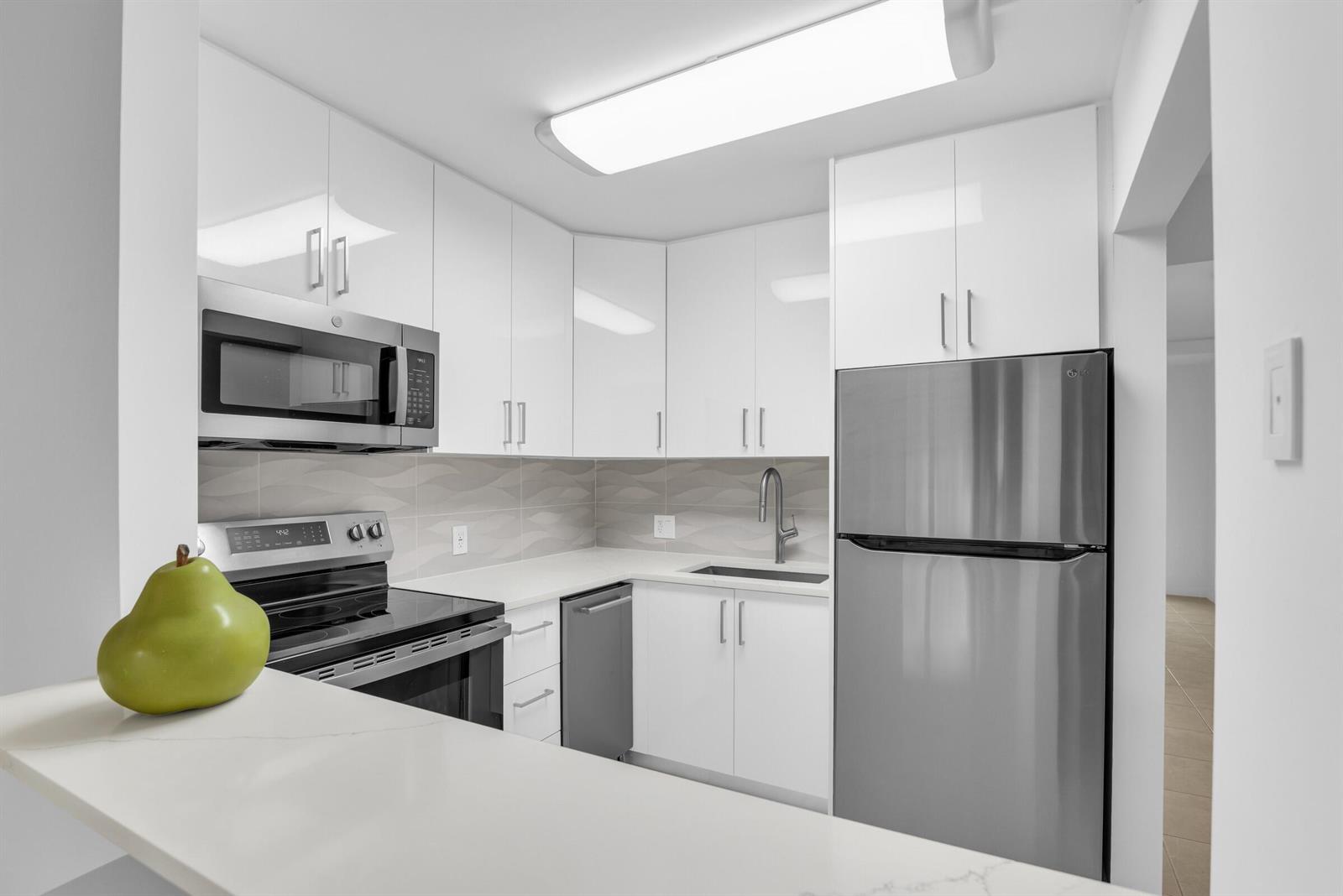 A modern kitchen features white cabinets, stainless steel appliances, and a light-colored countertop — 175 Fanshaw E, Boca Raton FL 33434, BOCA RATON, FL