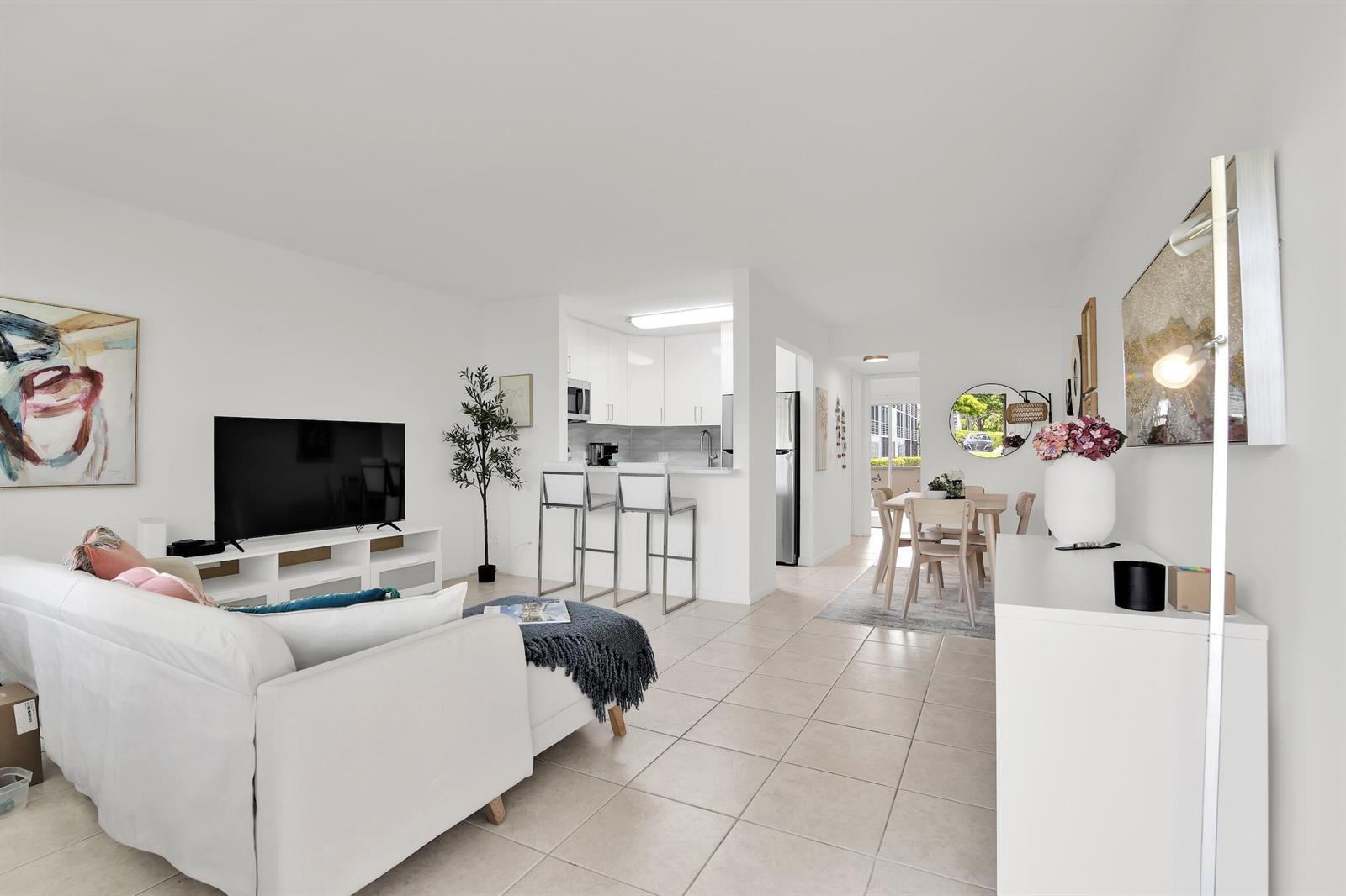 A bright living room with white tile floors, a kitchen breakfast bar, and dining area — 175 Fanshaw E, Boca Raton FL 33434, BOCA RATON, FL