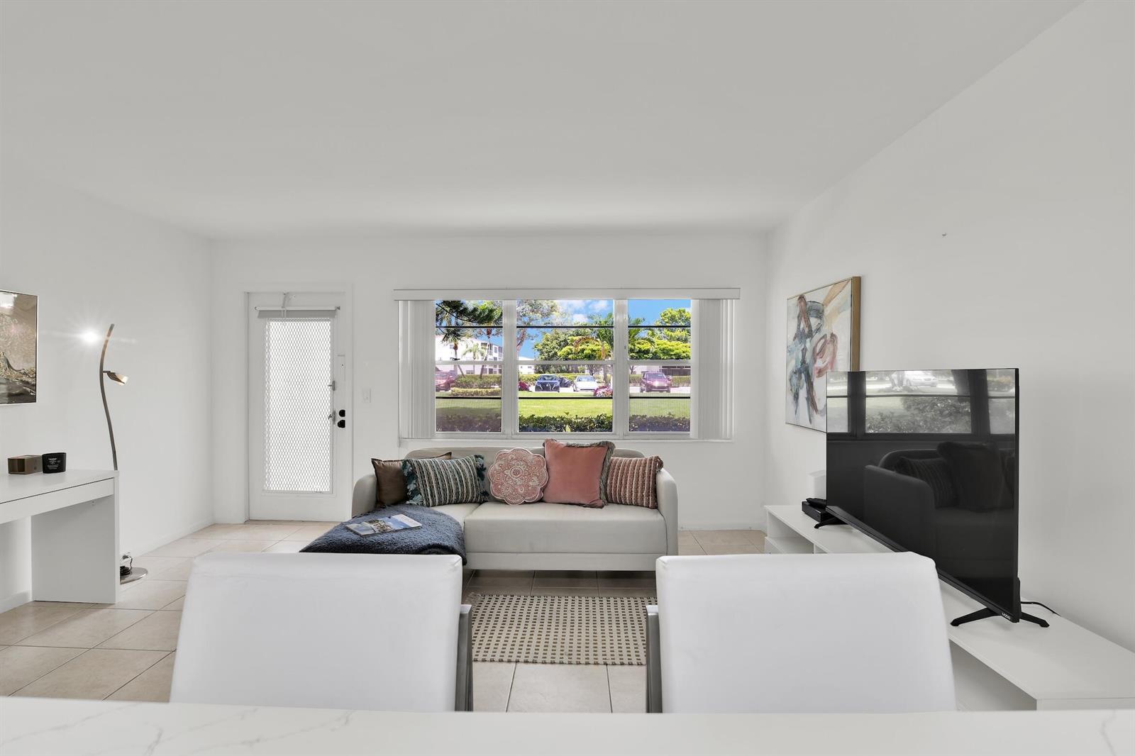 A bright living room features a white sofa, a television, and a large window view — 175 Fanshaw E, Boca Raton FL 33434, BOCA RATON, FL