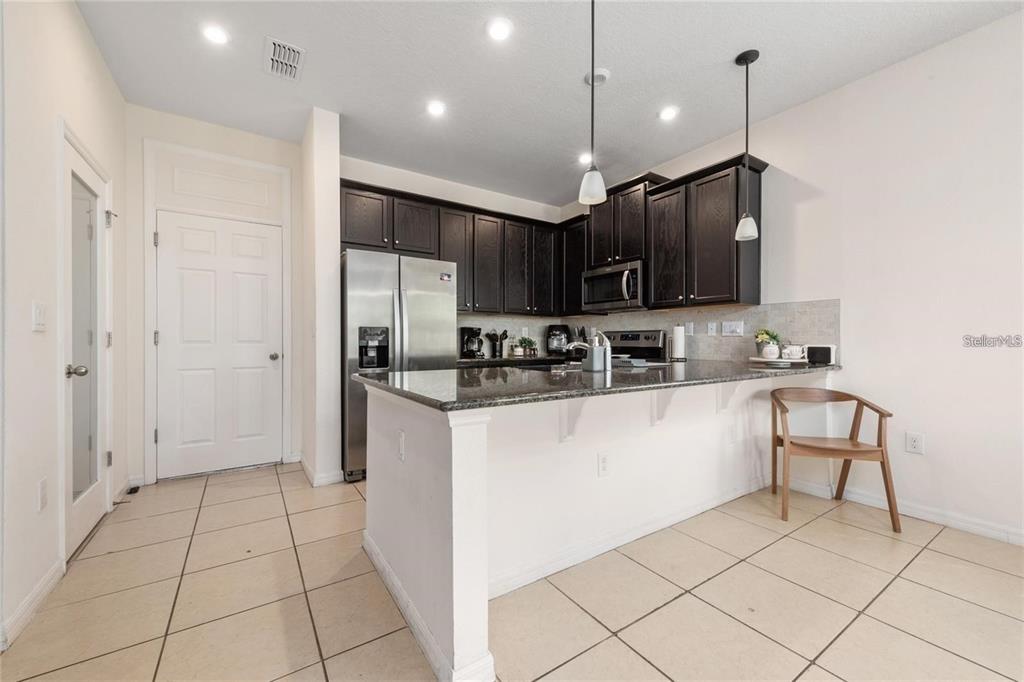 A kitchen features dark wood cabinets, granite countertops, stainless steel appliances, and tile flooring — 2449 VARENNA LOOP, KISSIMMEE, FL