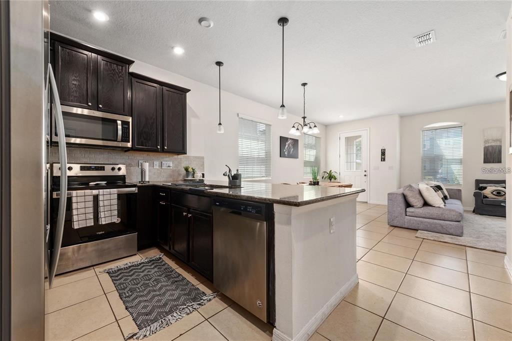 A kitchen with dark cabinets and stainless steel appliances opens into a living room area — 2449 VARENNA LOOP, KISSIMMEE, FL