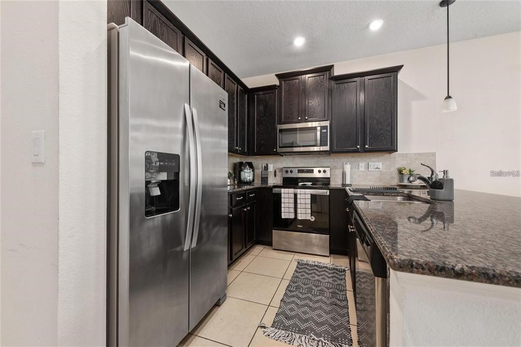 A kitchen features dark wood cabinets, stainless steel appliances, and granite countertops — 2449 VARENNA LOOP, KISSIMMEE, FL