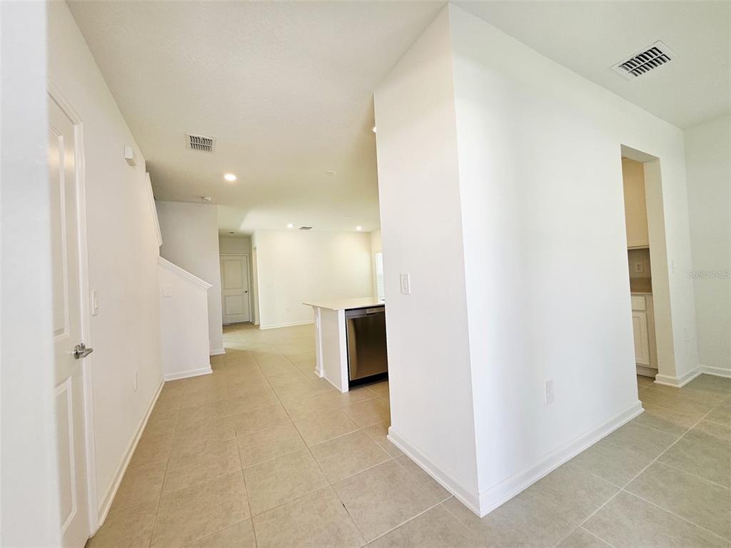 A bright, open-concept interior features light tile flooring, white walls, and a kitchen island — 6072 ZEN WAY, CLERMONT, FL