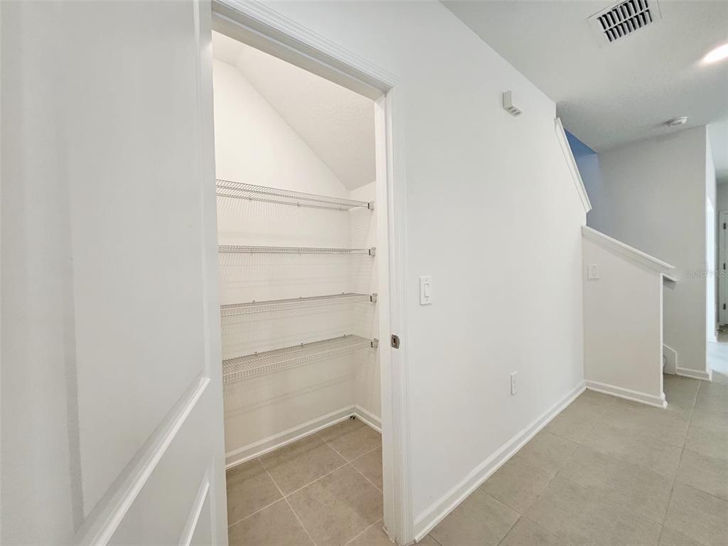 A white pantry with wire shelving sits beside a hallway with tiled floors — 6072 ZEN WAY, CLERMONT, FL