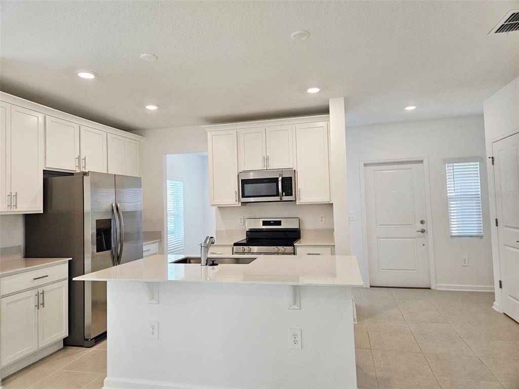 A modern kitchen features white cabinetry, stainless steel appliances, and a central island with seating — 6072 ZEN WAY, CLERMONT, FL