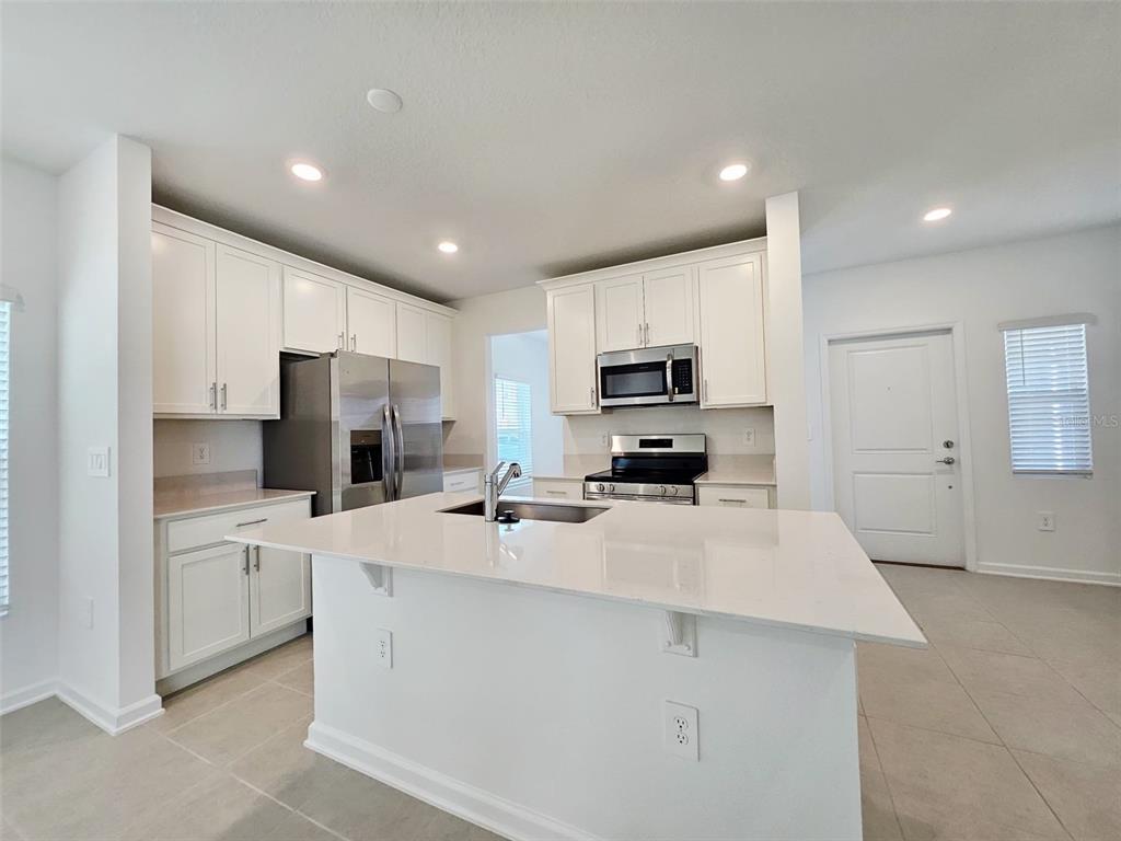 A modern kitchen features white cabinets, stainless steel appliances, and a large central island — 6072 ZEN WAY, CLERMONT, FL