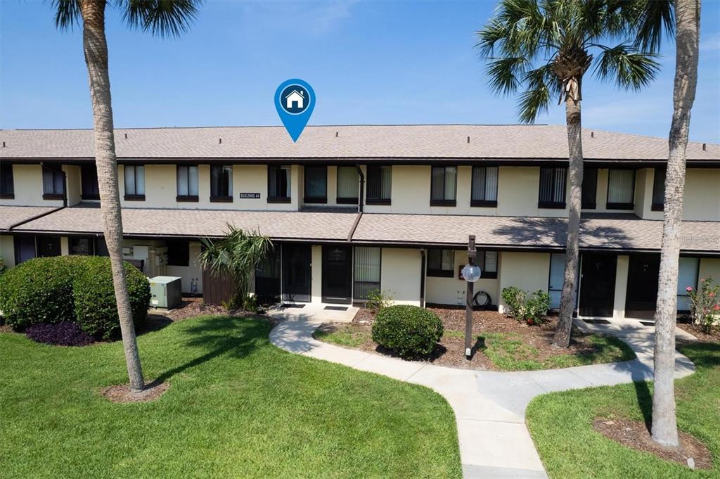 An exterior view of a two-story apartment building with palm trees and a walkway — 44 CLUB HOUSE DRIVE UNIT 105, PALM COAST, FL