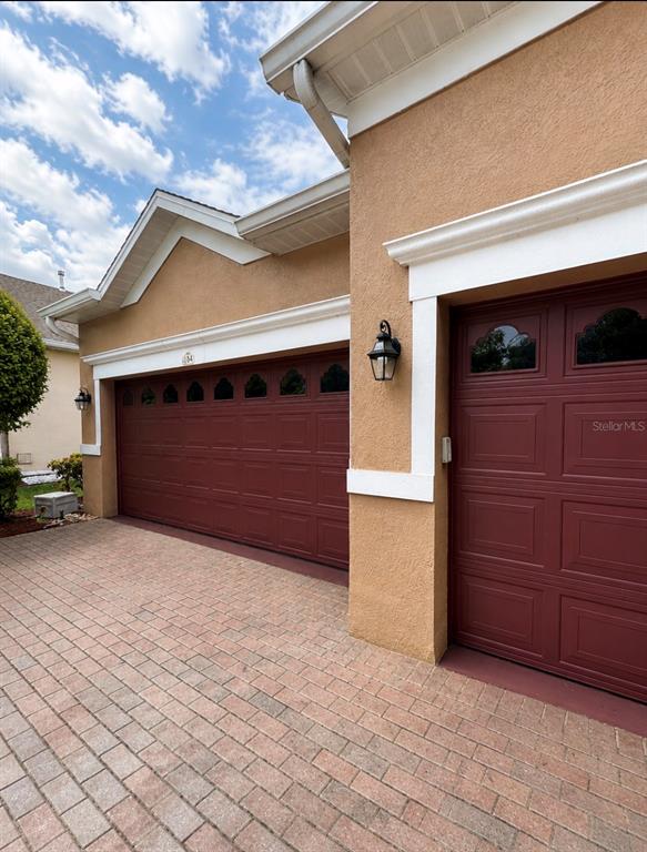 A tan stucco house exterior features a red two-car garage door and brick driveway — 184 CREPE MYRTLE DRIVE, GROVELAND, FL
