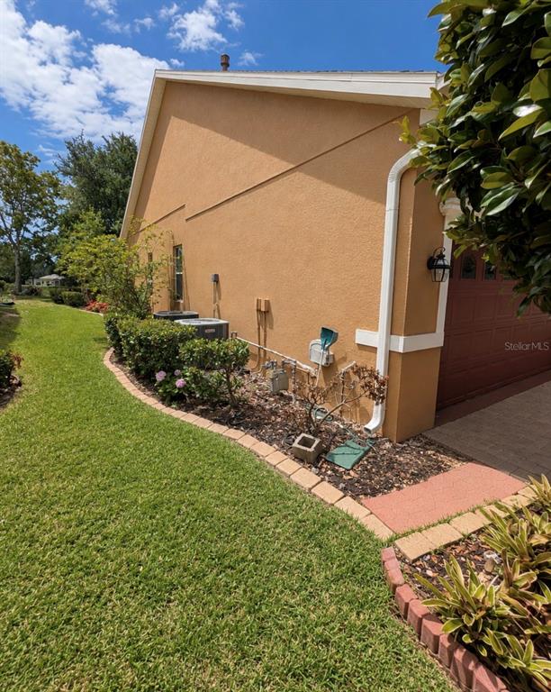 The side exterior of a tan stucco house features air conditioning units and landscaping — 184 CREPE MYRTLE DRIVE, GROVELAND, FL