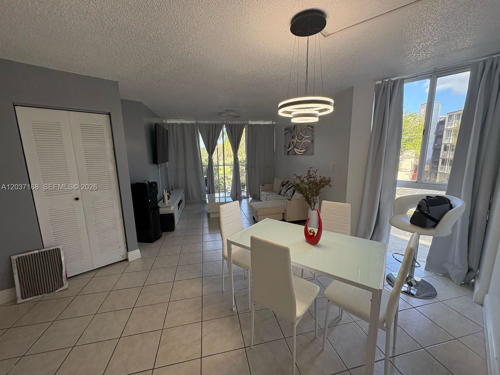 A dining area with a glass table and modern chandelier opens into a living room — 7035 NW 186th St # D302, Hialeah FL 33015, HIALEAH, FL