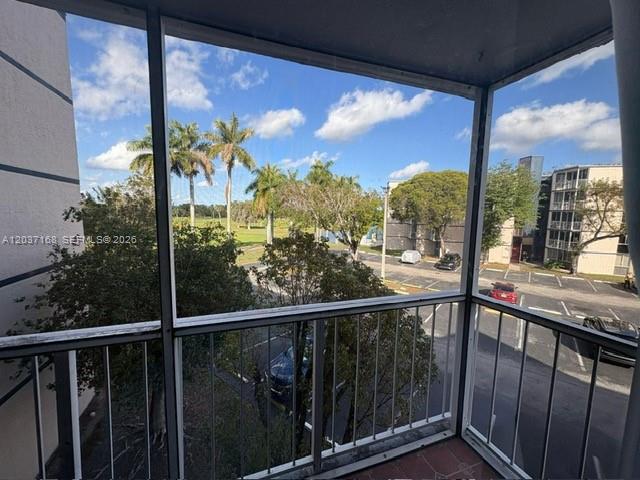 A view from a screened-in balcony overlooking a parking lot, trees, and nearby apartment buildings — 7035 NW 186th St # D302, Hialeah FL 33015, HIALEAH, FL