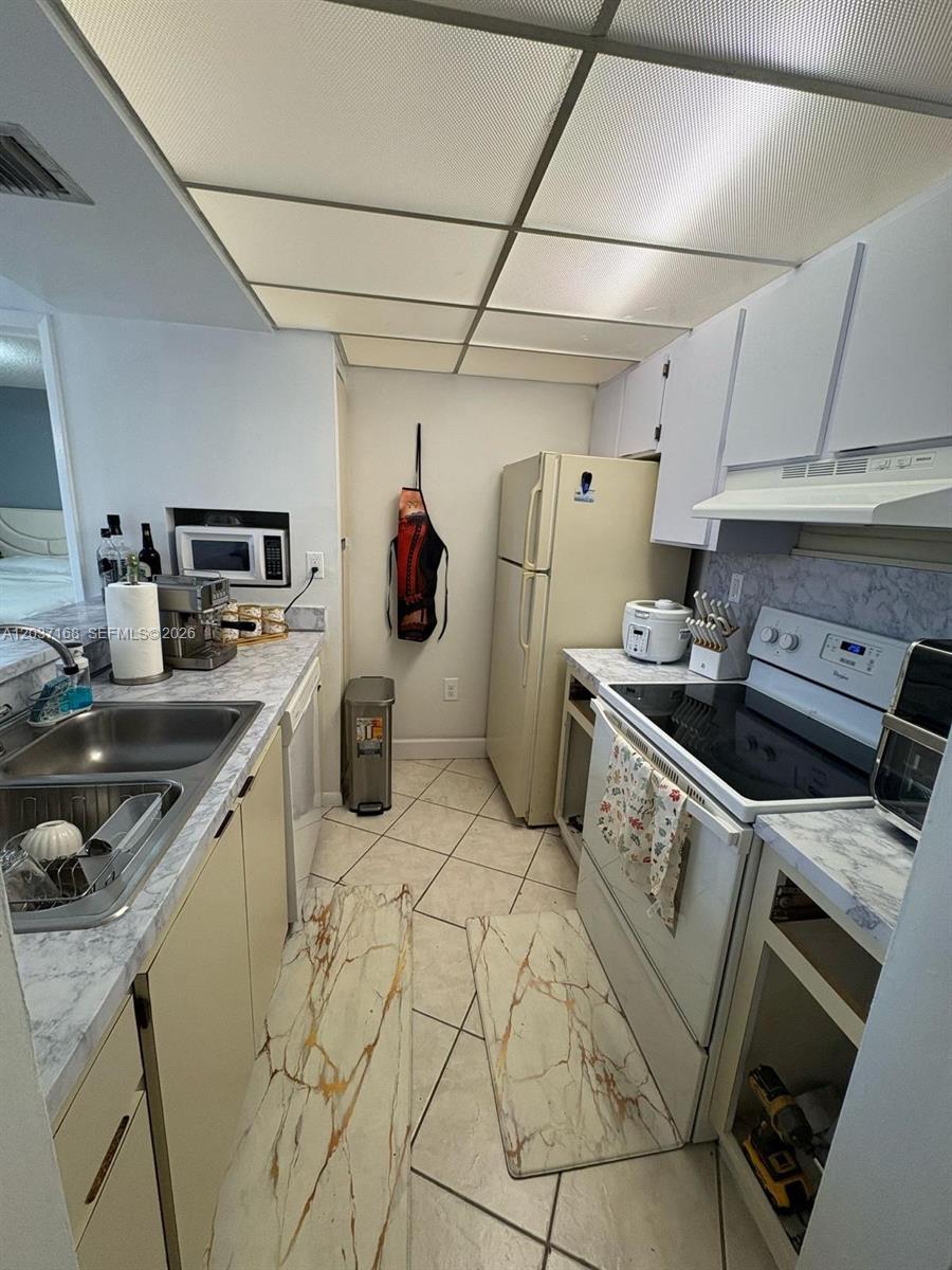 A kitchen features light-colored cabinets, marble-patterned countertops, a white stove, and a refrigerator — 7035 NW 186th St # D302, Hialeah FL 33015, HIALEAH, FL