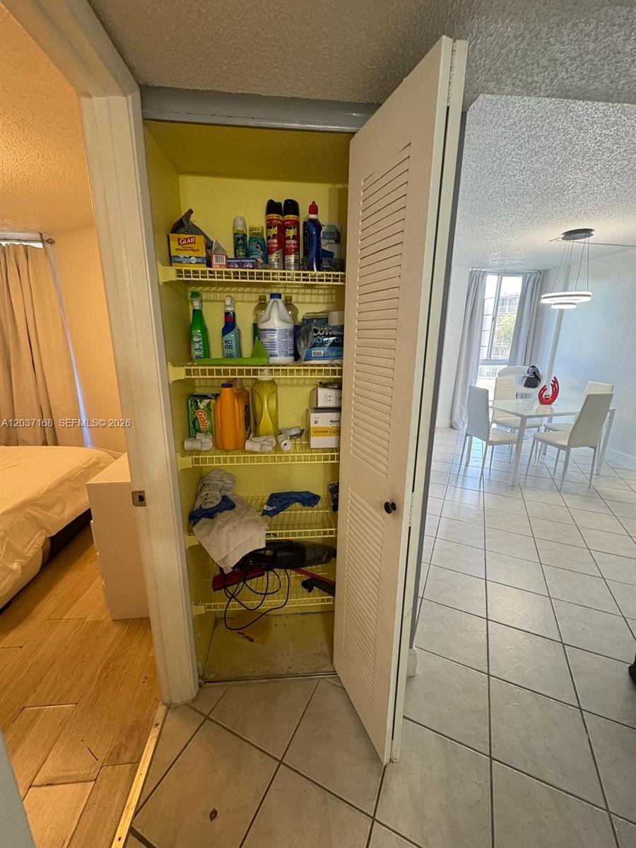 A closet with wire shelving containing cleaning supplies stands between a bedroom and dining area — 7035 NW 186th St # D302, Hialeah FL 33015, HIALEAH, FL