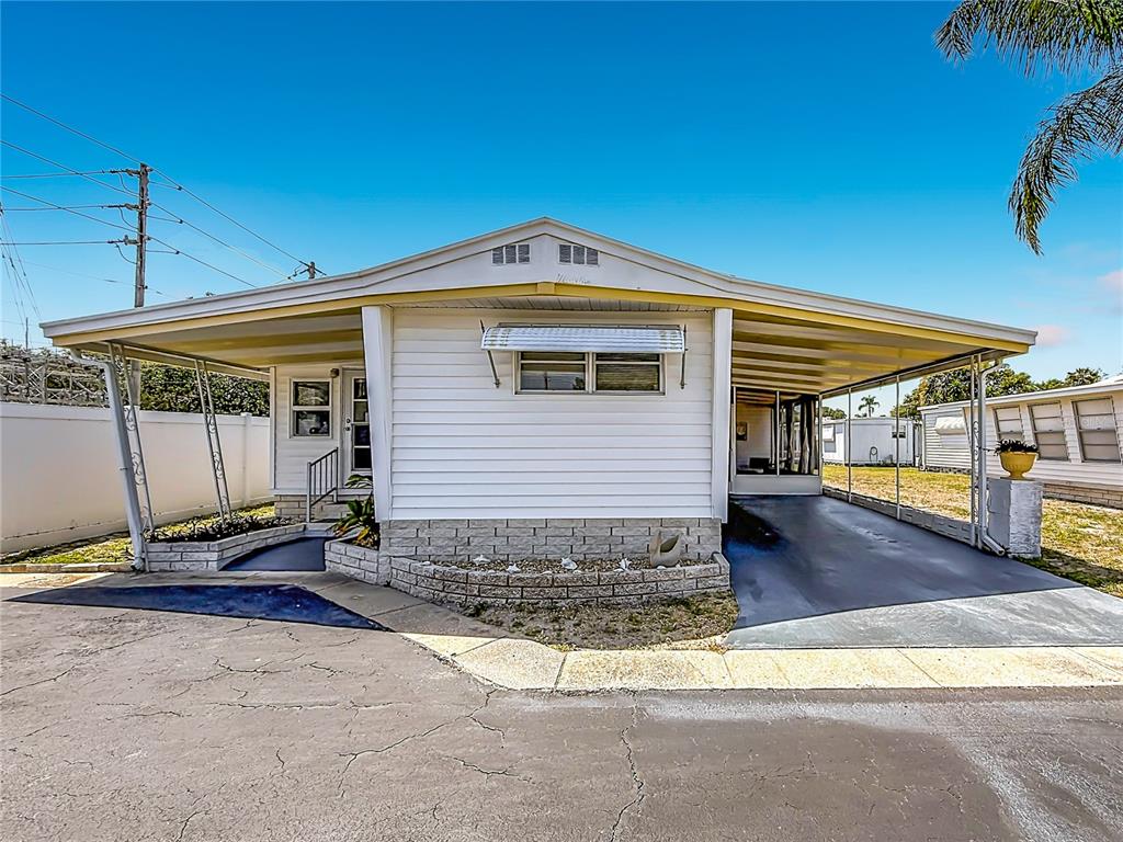 A single-story manufactured home with a white exterior, a carport, and a stone-veneer base — 1040 MAIN STREET UNIT 162, DUNEDIN, FL