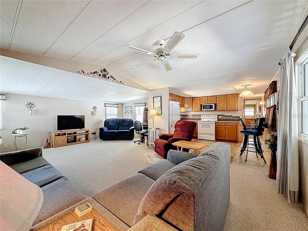 An open-concept living room and kitchen area with carpeted floors and light-colored walls — 1040 MAIN STREET UNIT 162, DUNEDIN, FL