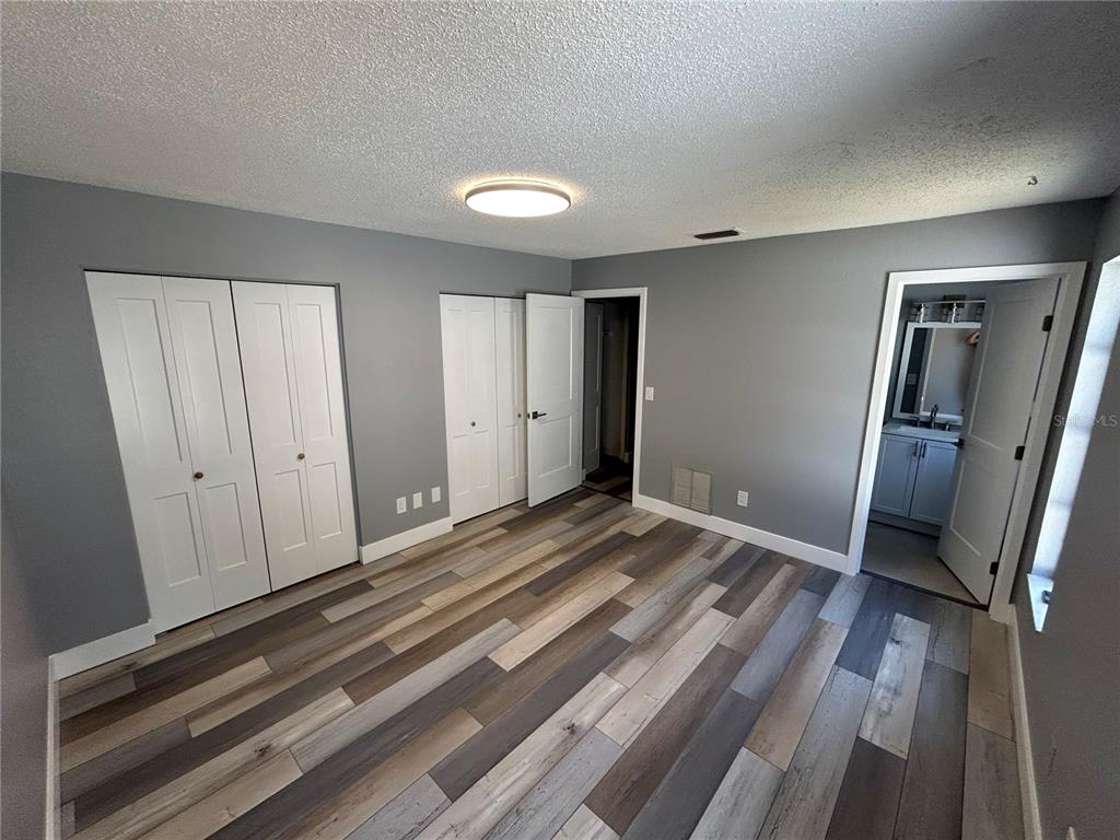 A bedroom with gray walls, wood-look flooring, two sets of closet doors, and an attached bathroom — 5708 27 TH AVENUE S, GULFPORT, FL