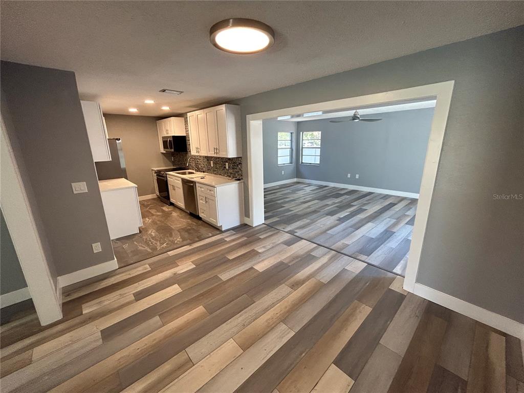 An open-concept kitchen with white cabinets and wood-look flooring connects to a living area — 5708 27 TH AVENUE S, GULFPORT, FL