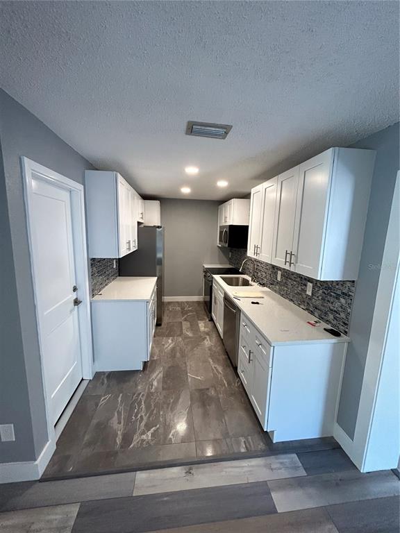 A galley kitchen features white cabinets, quartz countertops, a tiled backsplash, and gray marble flooring — 5708 27 TH AVENUE S, GULFPORT, FL