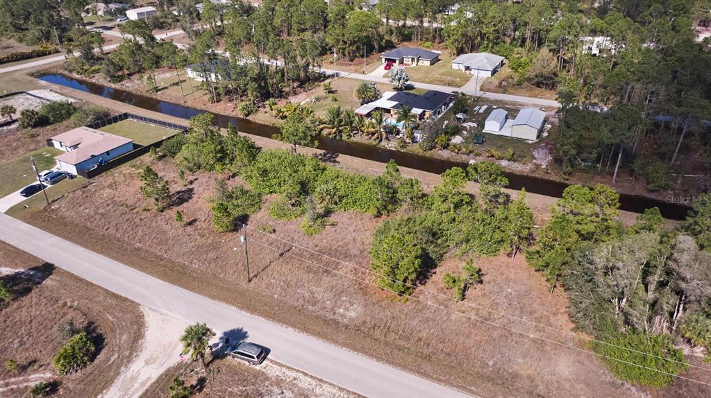 An aerial view shows a vacant lot with trees and brush bordering a canal — 1025 WINTERS STREET E, LEHIGH ACRES, FL