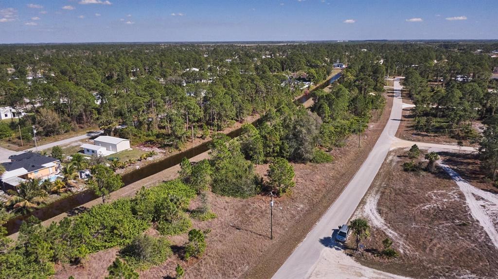 An aerial view shows a canal running between a residential street and wooded land — 1025 WINTERS STREET E, LEHIGH ACRES, FL