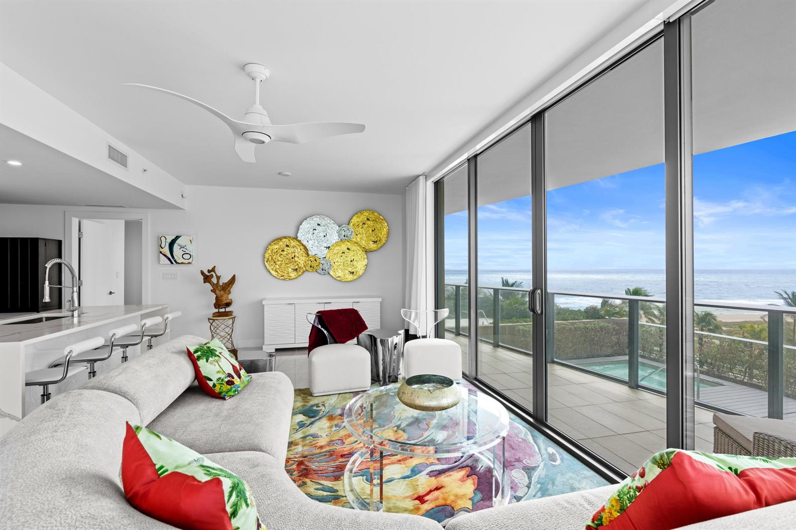 A modern living room with a curved sofa, colorful rug, and floor-to-ceiling ocean view windows — 730 N Ocean Boulevard # 505, Pompano Beach FL 33062, POMPANO BEACH, FL