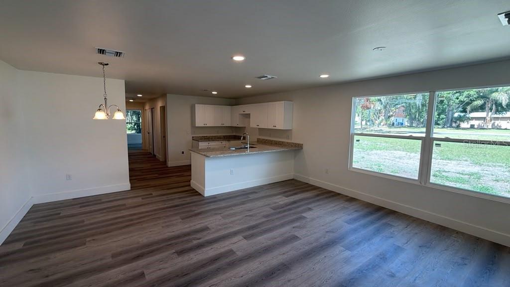 An open-concept kitchen and living area features wood-look flooring, white cabinets, and large windows — 638 W 7TH STREET, LAKELAND, FL