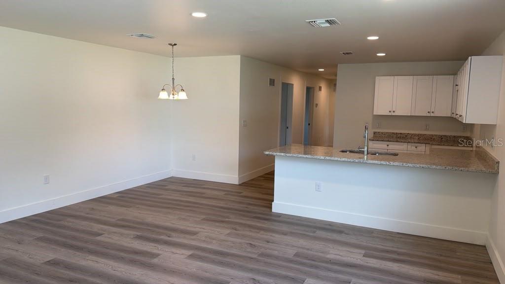 An open-concept kitchen and dining area features white cabinets, granite countertops, and wood-look flooring — 638 W 7TH STREET, LAKELAND, FL