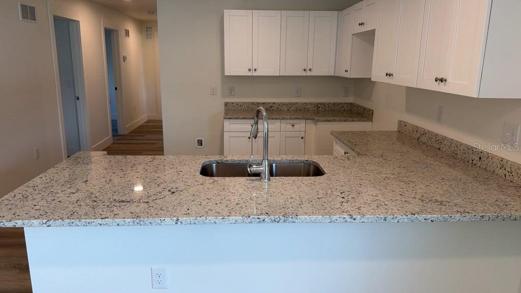 A kitchen features white cabinets, granite countertops, and a stainless steel sink on an island — 638 W 7TH STREET, LAKELAND, FL