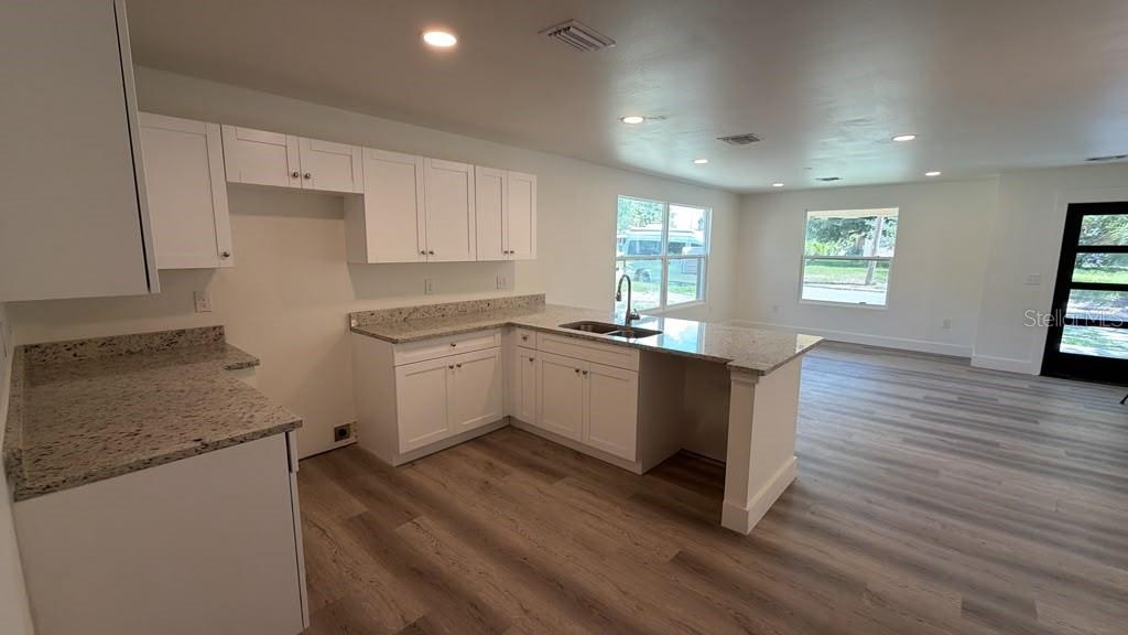 A kitchen with white cabinets, granite countertops, and wood-look flooring opens to a living area — 638 W 7TH STREET, LAKELAND, FL
