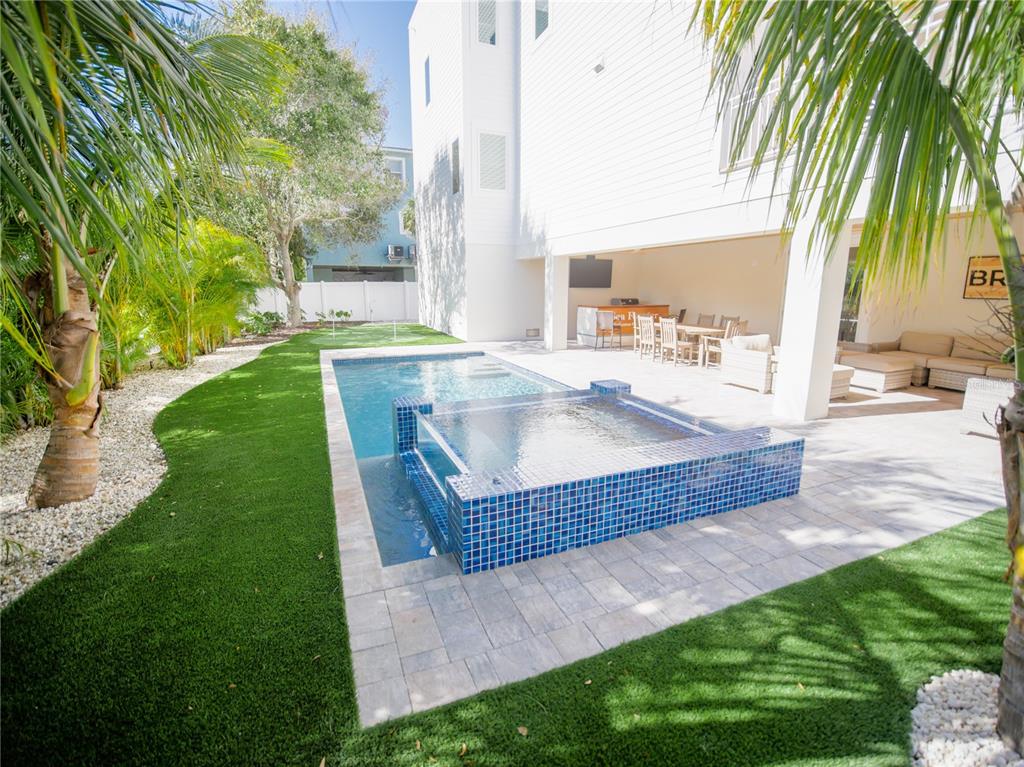 A backyard features a rectangular swimming pool with an attached tiled spa and artificial turf — 111 6TH STREET N, BRADENTON BEACH, FL