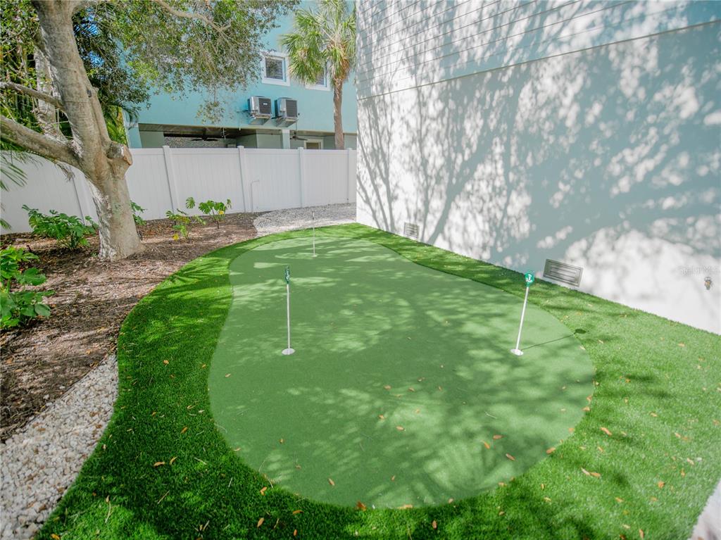 A backyard putting green with three holes sits beside a white house and a fence — 111 6TH STREET N, BRADENTON BEACH, FL