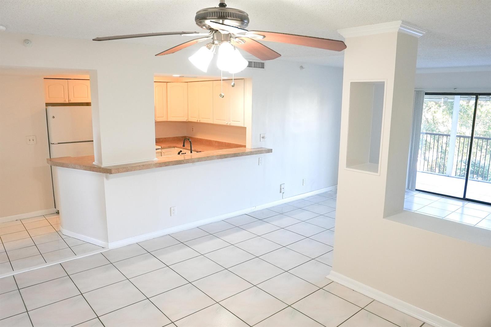 An open-concept kitchen with white cabinets and a breakfast bar overlooks a tiled living area — 2112 S Cypress Bend Drive # 404, Pompano Beach FL 33069, POMPANO BEACH, FL