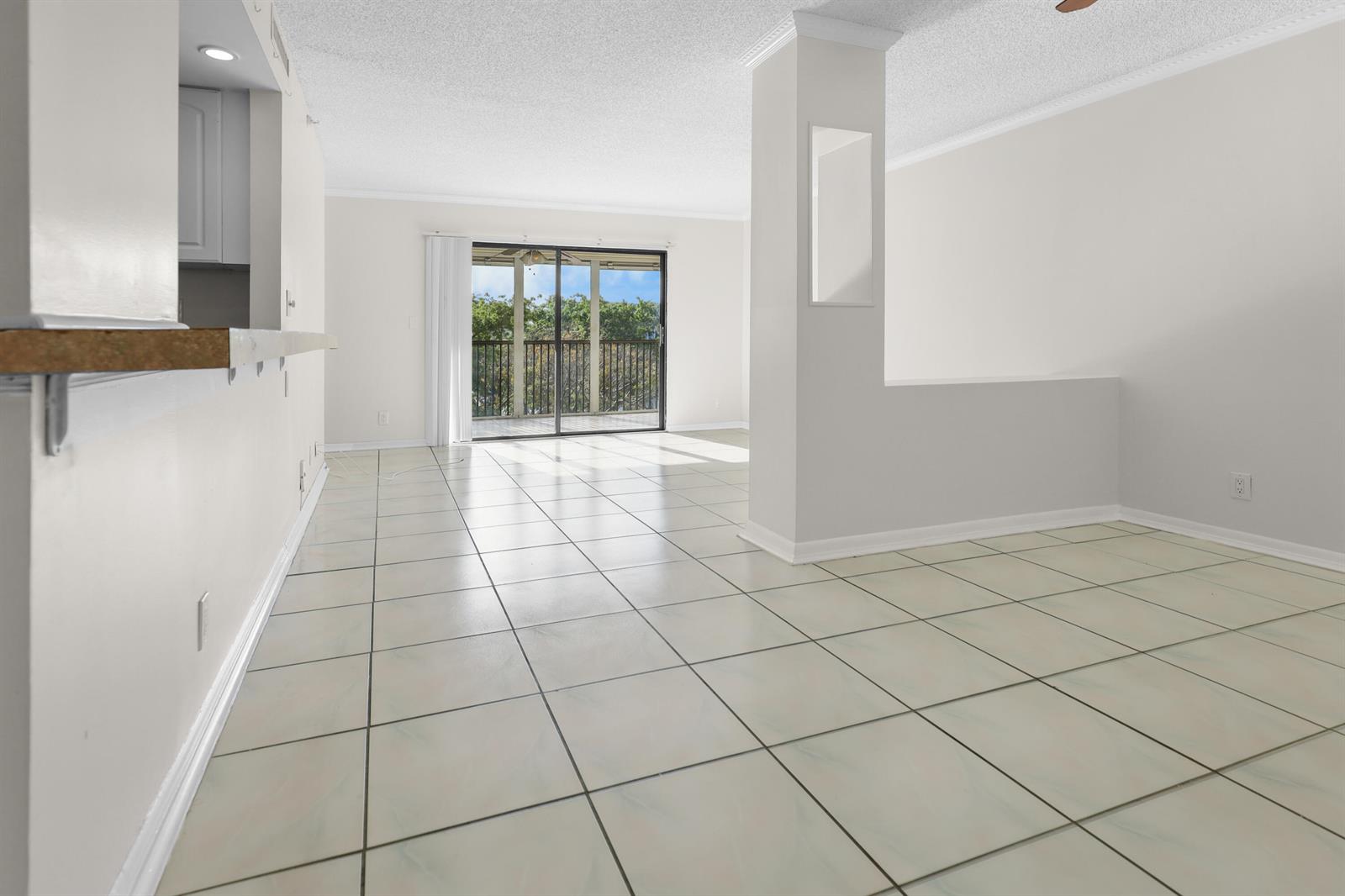 An empty living area features white tile floors, a central pillar, and a sliding glass door — 2112 S Cypress Bend Drive # 404, Pompano Beach FL 33069, POMPANO BEACH, FL