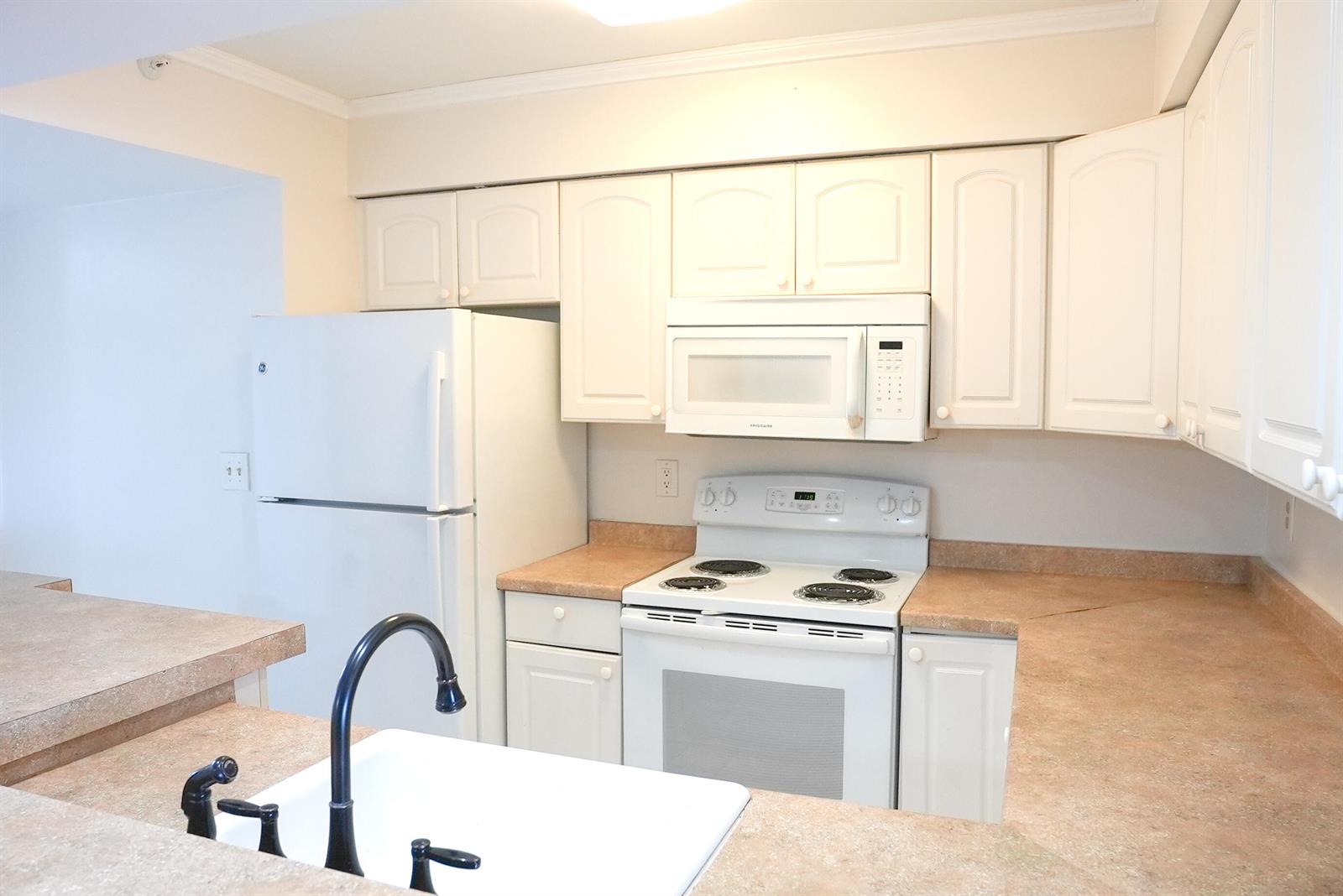 A kitchen features white cabinets, white appliances, and tan laminate countertops — 2112 S Cypress Bend Drive # 404, Pompano Beach FL 33069, POMPANO BEACH, FL