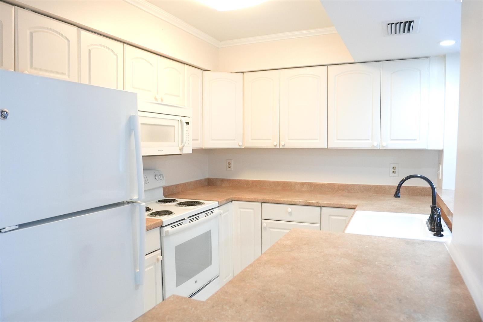 A kitchen features white cabinets, a white refrigerator, a white stove, and tan laminate countertops — 2112 S Cypress Bend Drive # 404, Pompano Beach FL 33069, POMPANO BEACH, FL