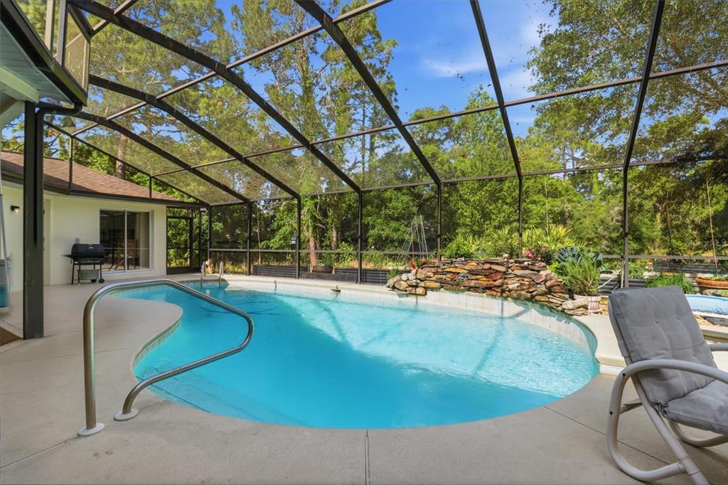 A screened-in swimming pool with a rock waterfall feature and a patio area — 3 PORTULACA COURT N, HOMOSASSA, FL