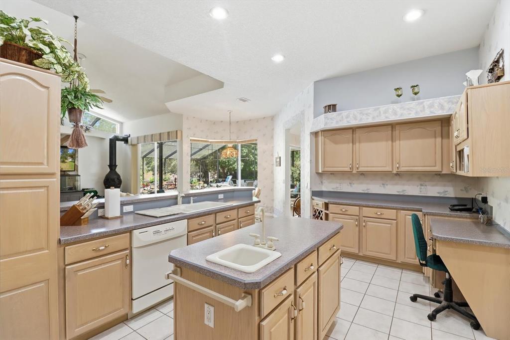 A kitchen features light wood cabinets, gray countertops, a center island, and tile flooring — 3 PORTULACA COURT N, HOMOSASSA, FL