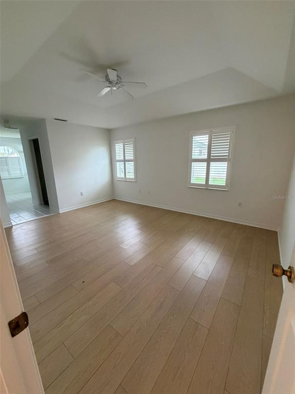 An empty bedroom features light wood-look flooring, a tray ceiling with a fan, and plantation shutters — 2 LAMAR LANE, PALM COAST, FL