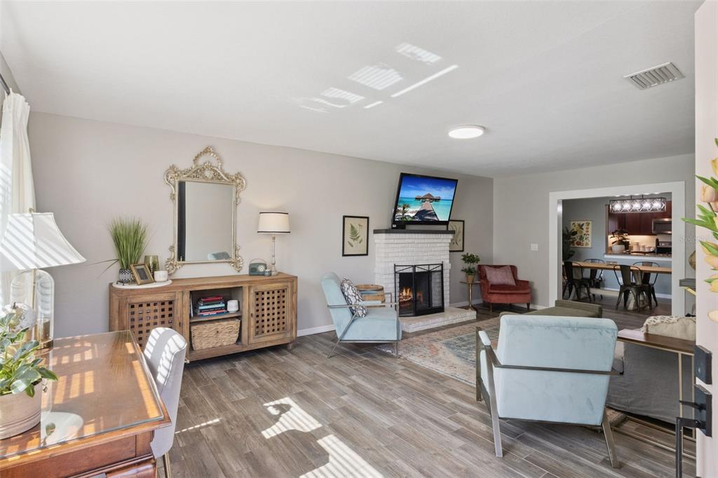 A living room with wood-look flooring, a white brick fireplace, and a dining area beyond — 415 8TH STREET NE, WINTER HAVEN, FL
