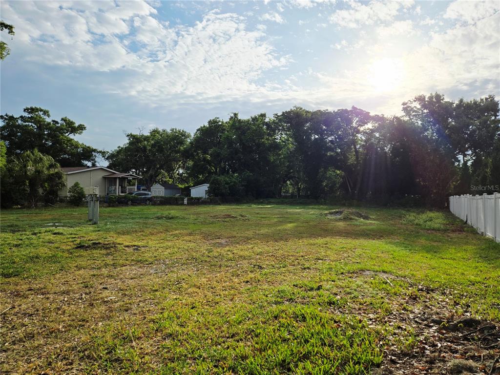 A large, grassy vacant lot is bordered by trees and a white fence — 14701 DEL VALLE ROAD, TAMPA, FL