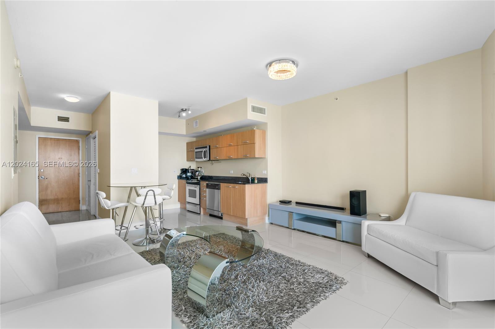 A living room features white sofas, a glass coffee table, and an open kitchen area — 350 S Miami Ave # 2515, Miami FL 33130, MIAMI, FL
