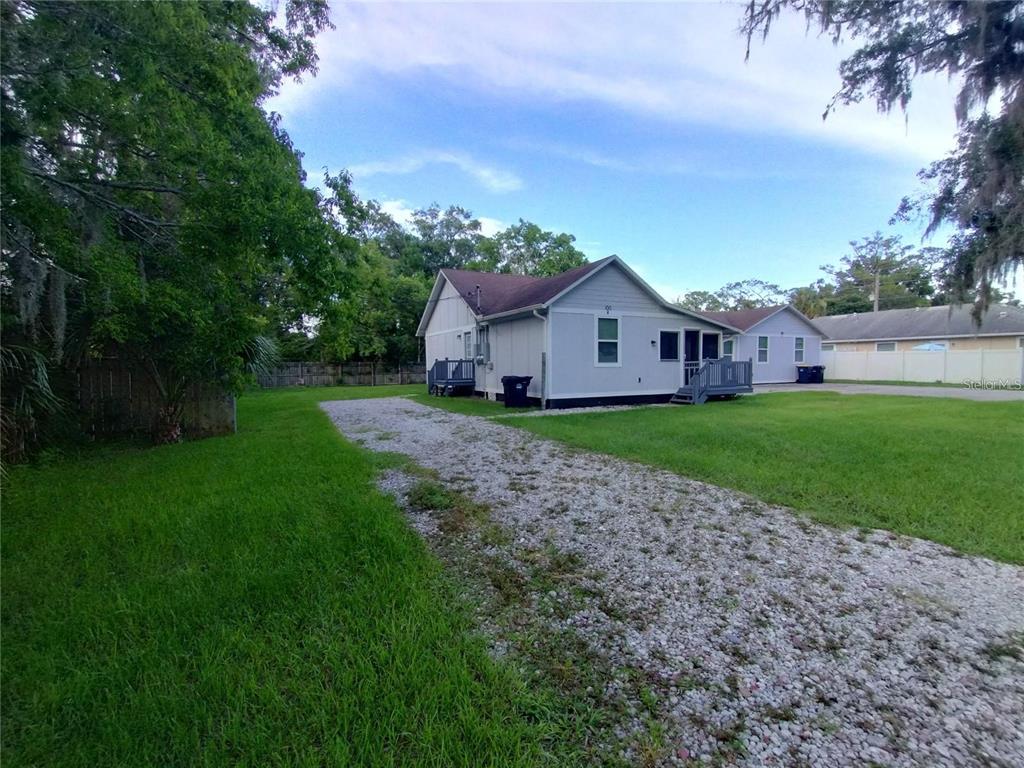 A gravel driveway leads to the side of a light-colored house with a small deck — 100 S STONE STREET UNIT A, BUNNELL, FL