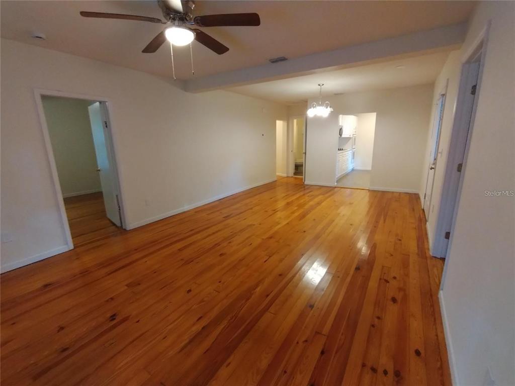 An empty room features polished hardwood floors, a ceiling fan, and a doorway to a kitchen — 100 S STONE STREET UNIT A, BUNNELL, FL
