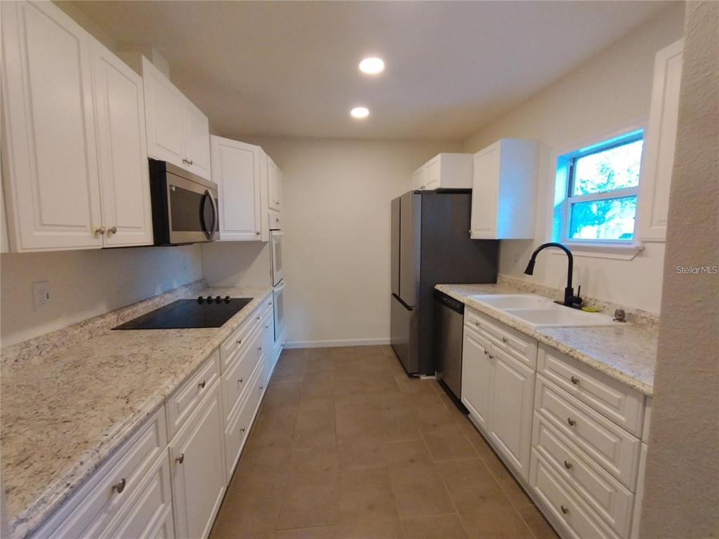 A kitchen features white cabinets, granite countertops, stainless steel appliances, and tile flooring — 100 S STONE STREET UNIT A, BUNNELL, FL