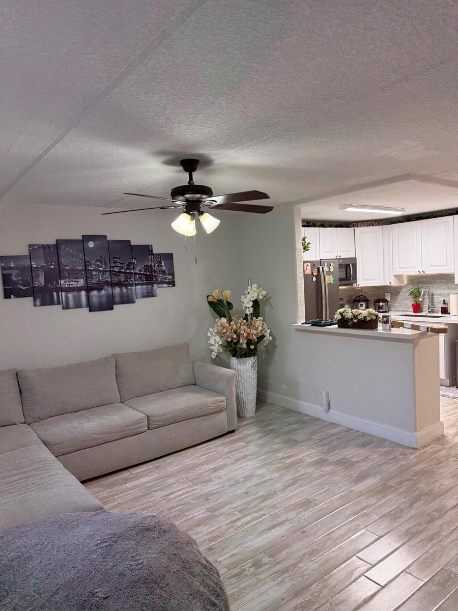 A living room with a sectional sofa, a city skyline wall art, and a kitchen pass-through — 2000 Springdale Boulevard # 108, Palm Springs FL 33461, PALM SPRINGS, FL