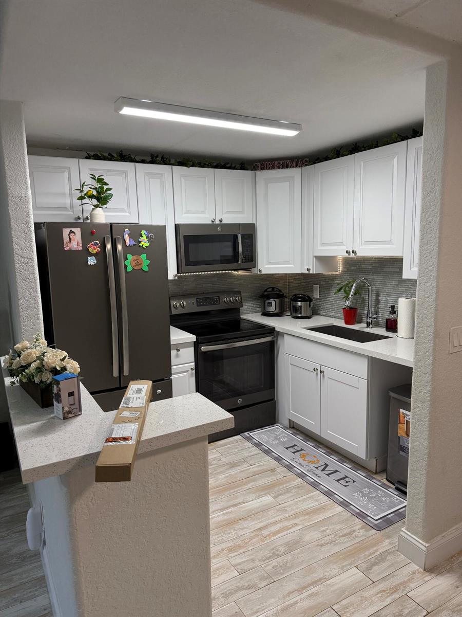 A kitchen features white cabinets, dark appliances, a light-colored countertop, and wood-look tile flooring — 2000 Springdale Boulevard # 108, Palm Springs FL 33461, PALM SPRINGS, FL