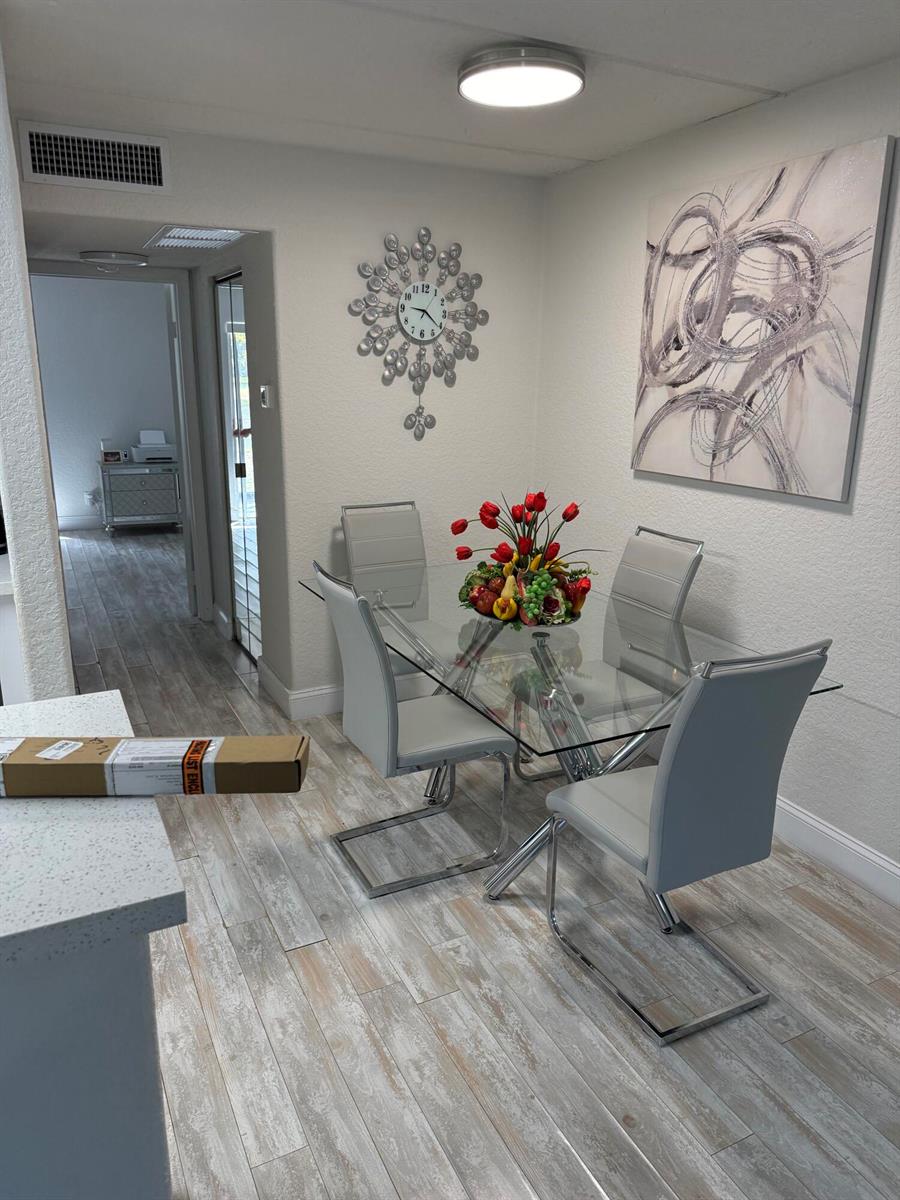 A dining area features a glass table, four gray chairs, wall art, and a clock — 2000 Springdale Boulevard # 108, Palm Springs FL 33461, PALM SPRINGS, FL
