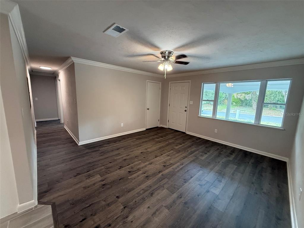 An empty living room features dark wood-look flooring, light gray walls, and a ceiling fan — 1239 SE 18TH TERRACE, GAINESVILLE, FL