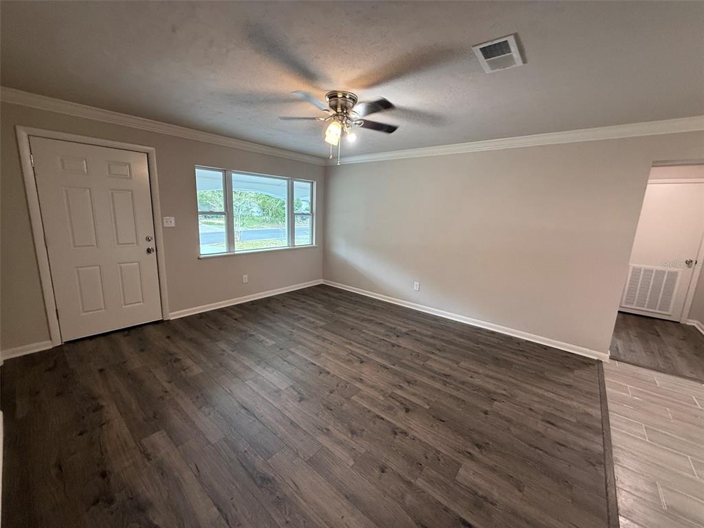 An empty living room features gray wood-look flooring, a ceiling fan, and a front door — 1239 SE 18TH TERRACE, GAINESVILLE, FL